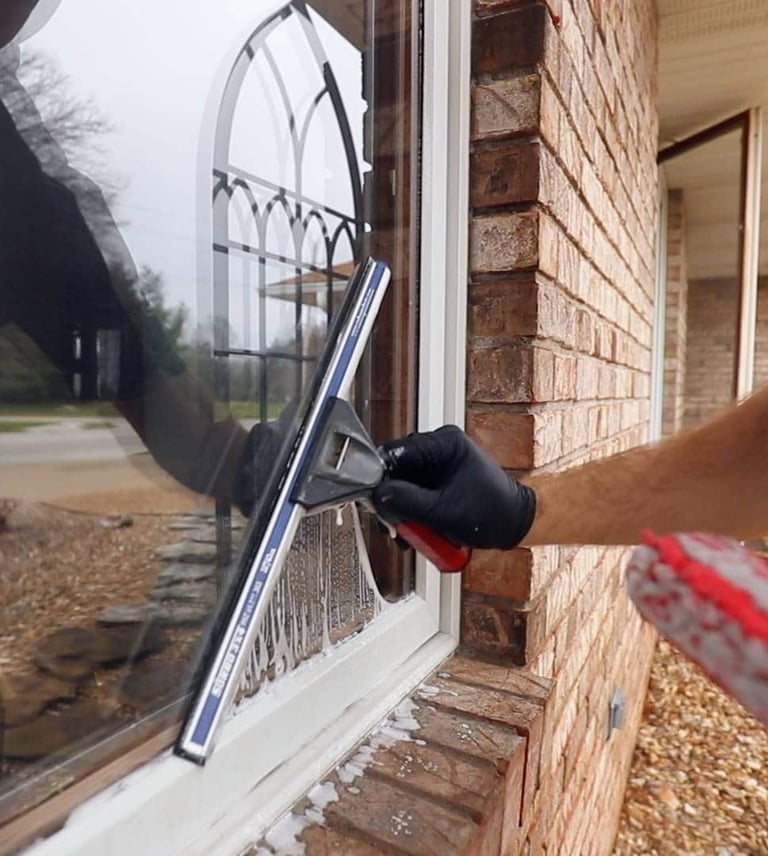 Hand in black glove cleaning exterior window with squeegee tool on brick house