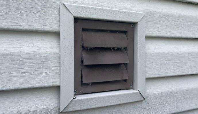 Exterior dryer vent with horizontal louvers mounted on white vinyl siding