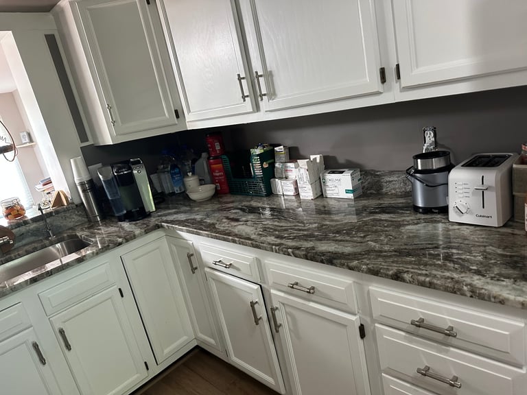 Modern kitchen with white cabinetry, gray marble countertops, black backsplash, and stainless steel appliances